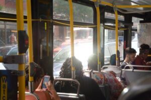 The interior of a full bus looking forward. Bright sun is reflecting in through the windows.