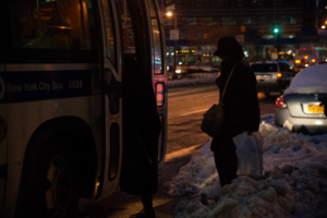 A person in the twilight getting ready to step onto a bus through a big bank of snow